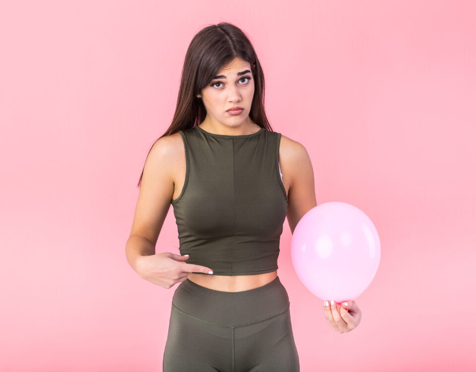 Beautiful young woman holding a pink balloon , feeling bloated concept , Woman having abdominal pain isolated on white